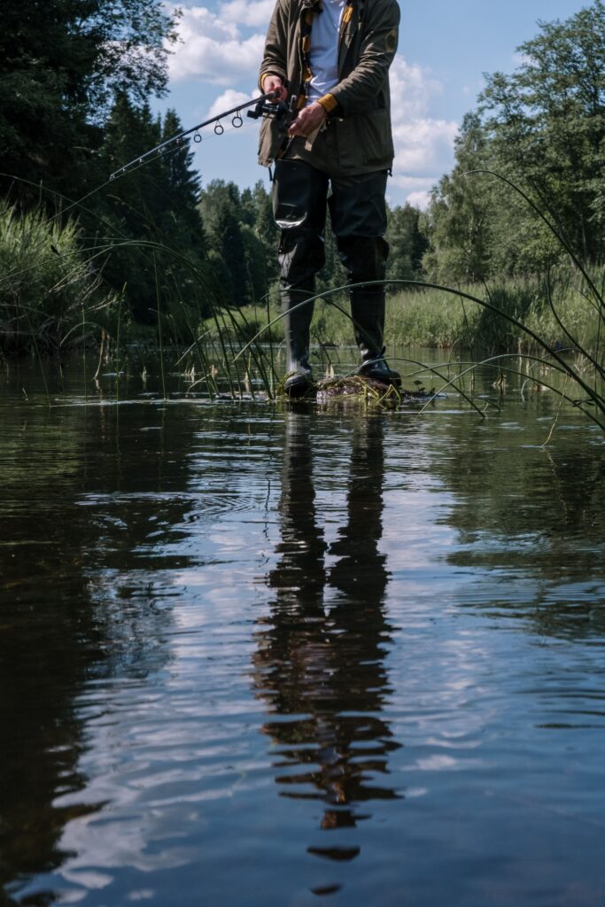 A person fishing in a serene river surrounded by lush greenery, reflecting on the calm water.